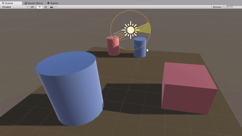 programa unity3d se observa una escena con un plano, un cubo y dos cilindros. El plano está pintado color marrón, hay dos cilindros azules, uno rojo y un cubo rojo, Además una fuente de luz direccional.